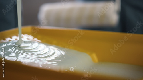 White paint spreading in yellow tray for paint roller on blurred background.