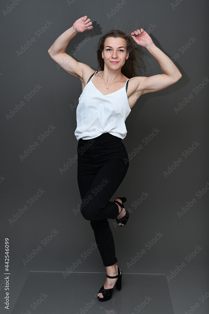 Full length studio portrait of cute caucasian girl in white blouse and black pants with smile posing on gray background