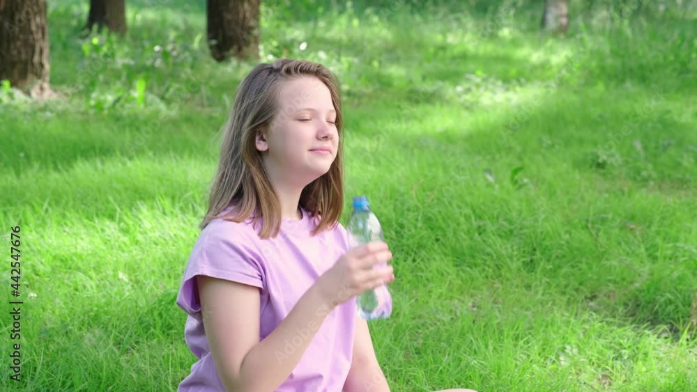 Teen girl drinking water from bottle in summer park. Drinking water in the heat concept Teen girl drinking water from bottle in summer park. Drinking water in the heat concept