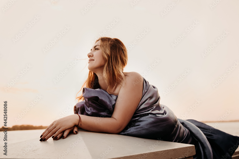 Beautiful young sexy woman wrapped in a blue blanket on the dawn near the water. Beautiful young sexy woman wrapped in a blue blanket on the dawn near the water.