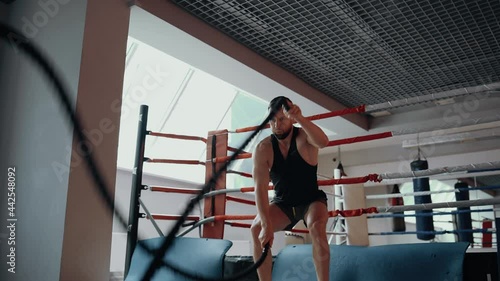 The close-up of the bearded man performing waves with fighting ropes in the gym. Intense masculine energy. Healthy lifestyle. Sport concept