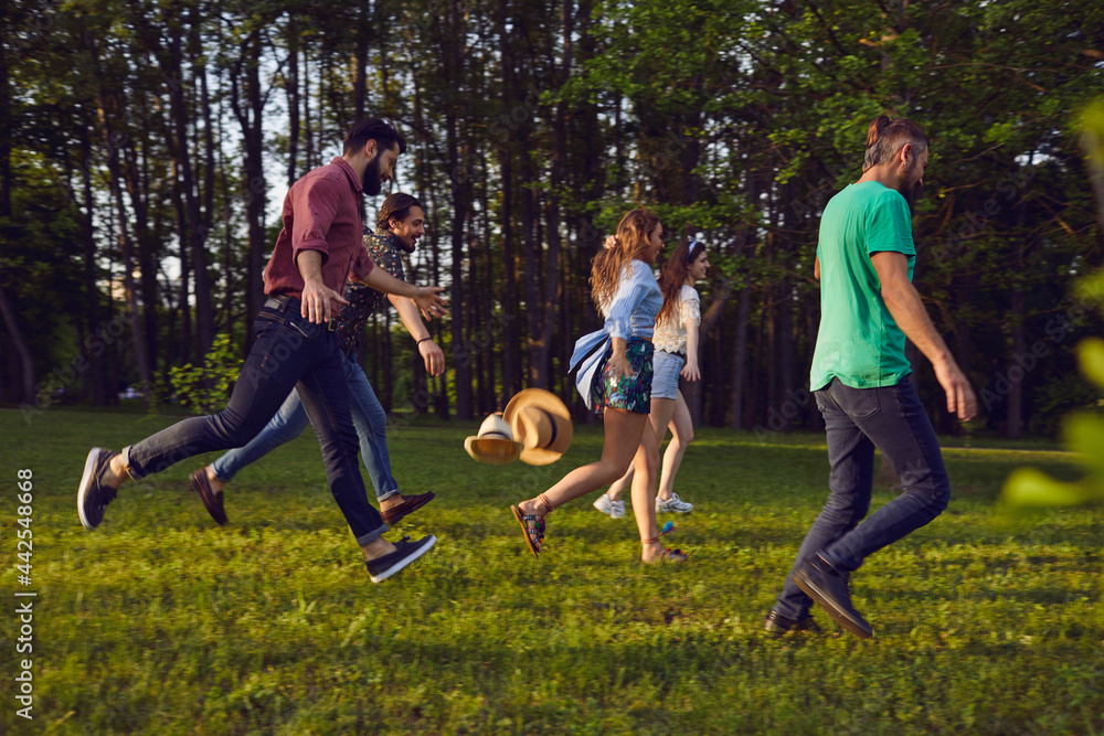 Fototapeta premium Group of happy young people running on grass in summer park. Youth on vacation.