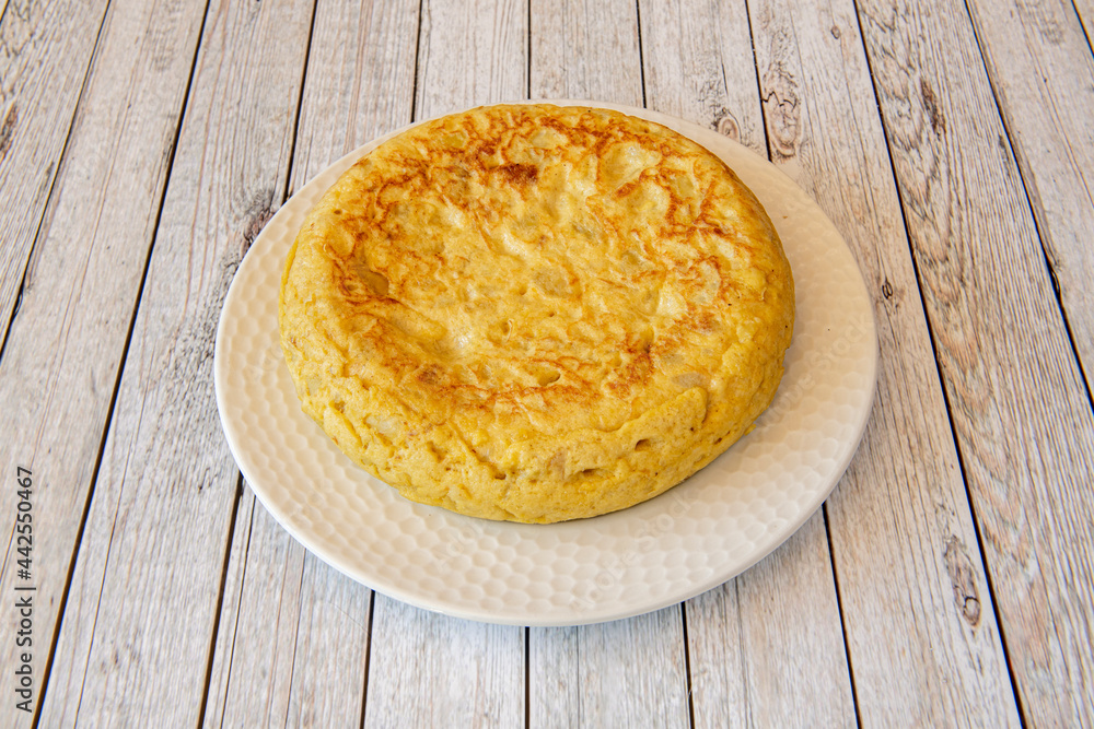 Spanish omelette with potatoes and eggs with a considerable thickness on a white plate and a light wood table Spanish omelette with potatoes and eggs with a considerable thickness on a white plate and a light wood table