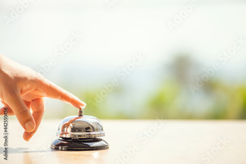 Woman ringing hotel bell of summer beach hotel front desk. Coastline sea and palm tree view. Travel concept.