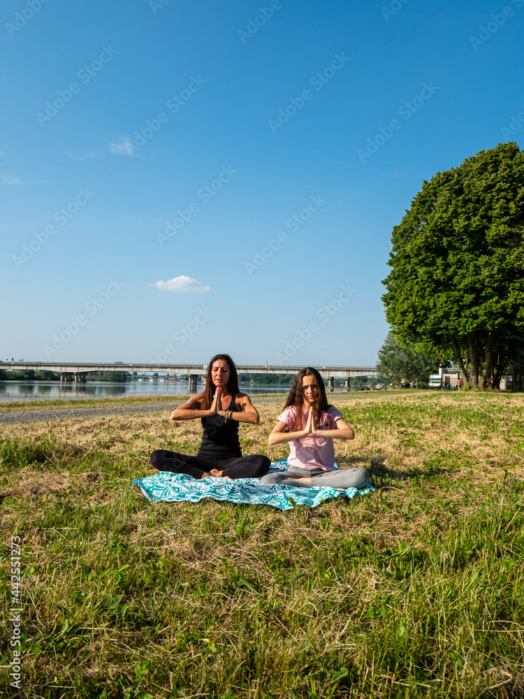 Naklejka one adult fit woman teaches yoga to a girl at the coastside, summer, in a park