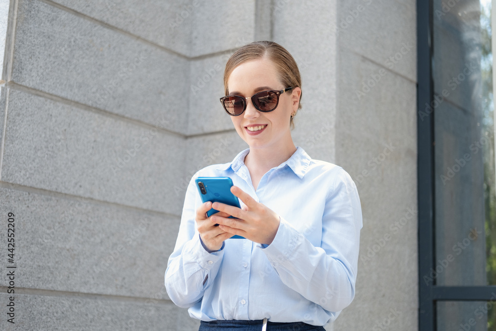 Fototapeta premium happy confident business woman typing on phone stand in city
