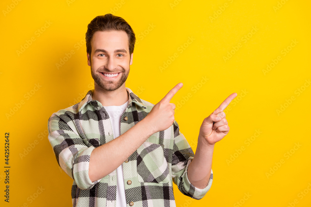 Photo of cheerful young happy positive man point finger empty space sale isolated on yellow color background Photo of cheerful young happy positive man point finger empty space sale isolated on yellow color background