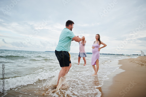 Summer vacations. Parents and people outdoor activity with children. Happy family holidays. Father, pregnant mother, baby daughter on sea sand beach.