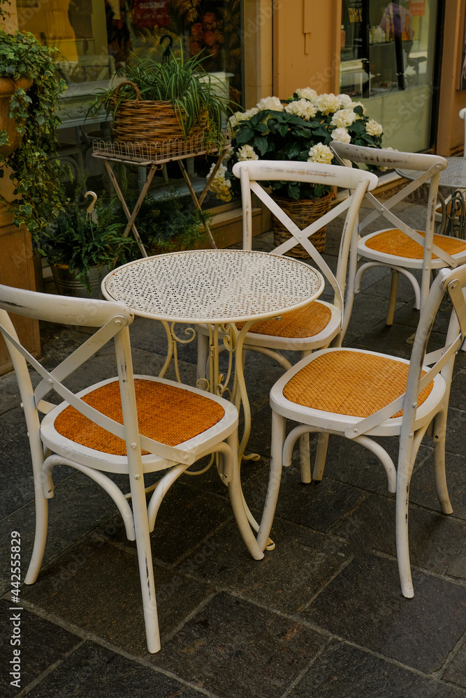 White wooden table with chairs across plants in pots in restaurant terrace. Cafe exterior. City life