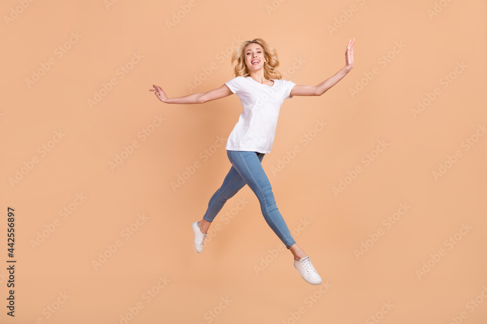 Photo of adorable shiny young lady wear white t-shirt smiling jumping high running isolated beige color background