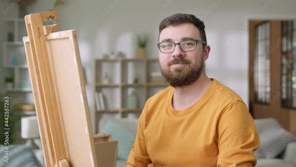 Young man is working in his modern home studio in the morning, drawing on canvas, enjoying the process of creating new artwork, inspired by natural beauty, Slow motion.
