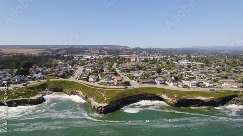 Long shot of drone flying along the cliffs of the small coastal town of Santa Cruz, CA. Cars driving along the ocean and people exersizing near the sea with aerial views of waves and cliffs in nature.