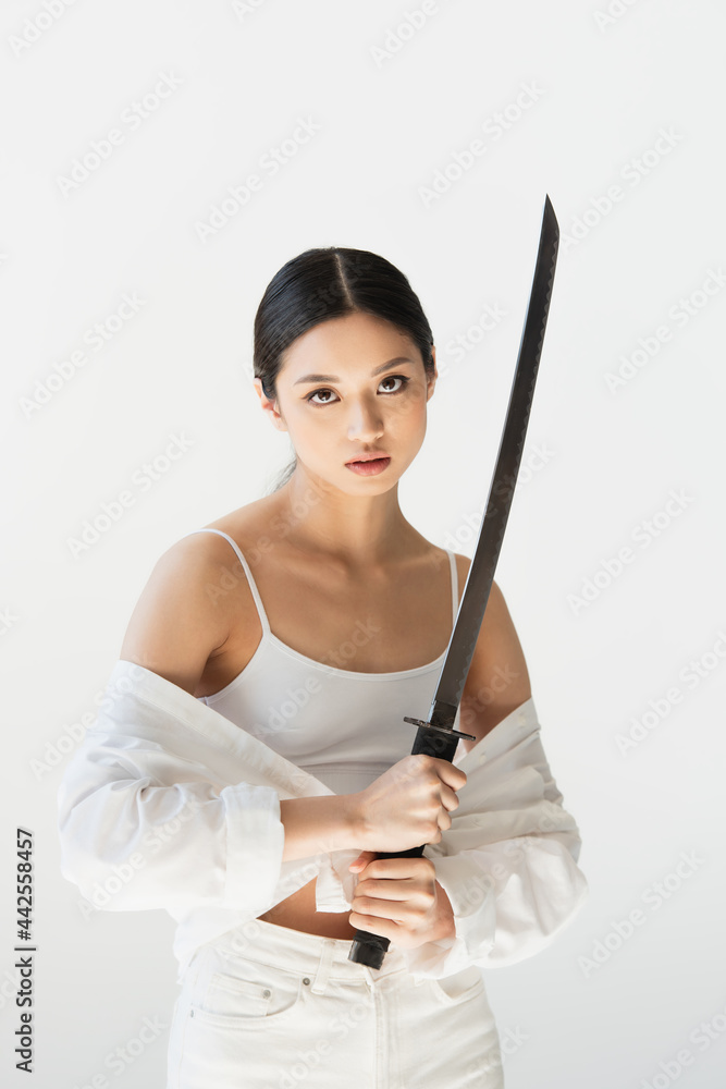 Asian woman in white clothes looking at camera while holding sword isolated on grey Asian woman in white clothes looking at camera while holding sword isolated on grey