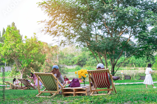 Back view of Asian senior lover sit to relax on garden chair and by the table in garden. Summer vacation in green surroundings. Happy person outdoors relaxing on deck chair in garden. Outdoor leisure.