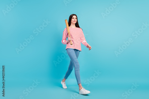 Full length body size view of attractive confident cheery girl walking carrying bat isolated over bright blue color background
