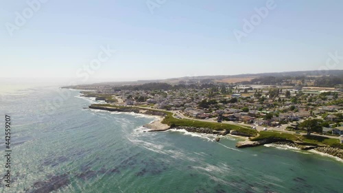 California coastline with epic views of the ocean and water with people living by the water. Waves crashing along coastal cliff edges with long drone shots and houses in a small town. 