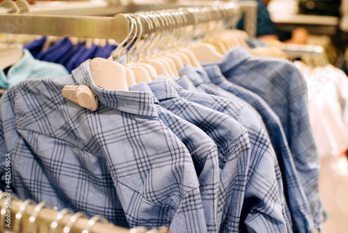 Cotton gray checkered shirts on hangers in supermarket close up, selective soft focus