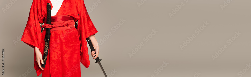 Cropped view of woman in oriental clothes holding sword isolated on grey, banner