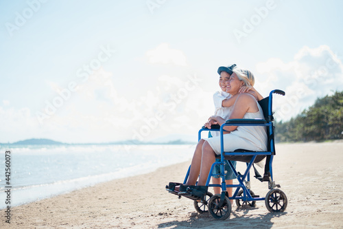 Grandchildren sit with the neighborhood on a wheelchair relaxing on the beach.