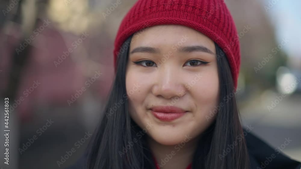 Headshot of young slim charming Asian woman in red hat looking at camera smiling standing outdoors on sunny spring autumn day. Close-up face of confident beautiful millennial posing Headshot of young slim charming Asian woman in red hat looking at camera smiling standing outdoors on sunny spring autumn day. Close-up face of confident beautiful millennial posing