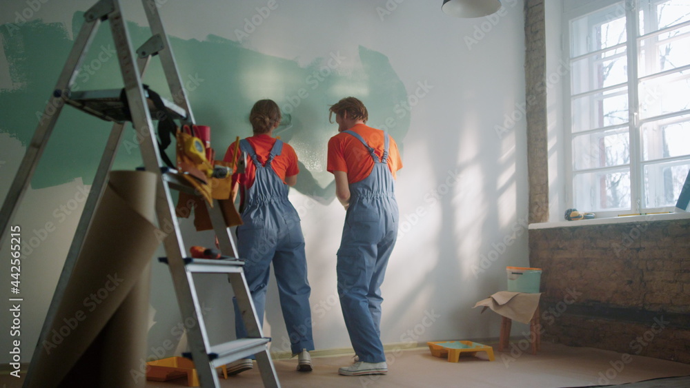 Happy couple painting wall indoors. Family dancing during decoration in home. Happy couple painting wall indoors. Family dancing during decoration in home.
