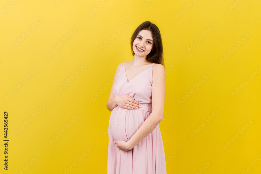Happy pregnant woman touching her abdomen at Colored background. Future mother. Expecting of a baby. Copy space Happy pregnant woman touching her abdomen at Colored background. Future mother. Expecting of a baby. Copy space