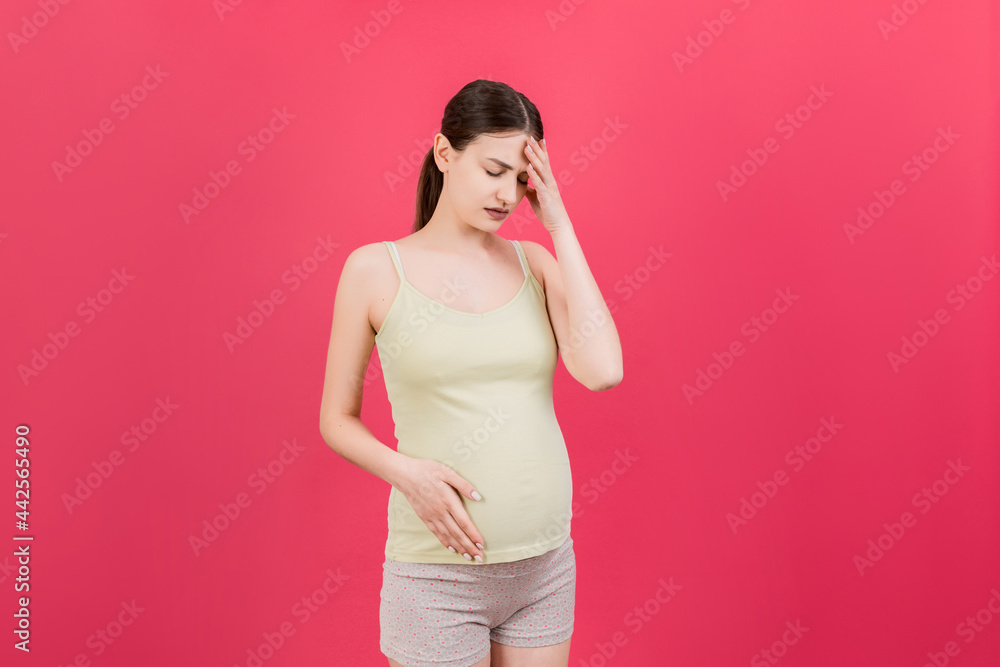 Beautiful young pregnant woman feeling head ache on colored background isolated. Stressed pregnant woman or mother problems Beautiful young pregnant woman feeling head ache on colored background isolated. Stressed pregnant woman or mother problems