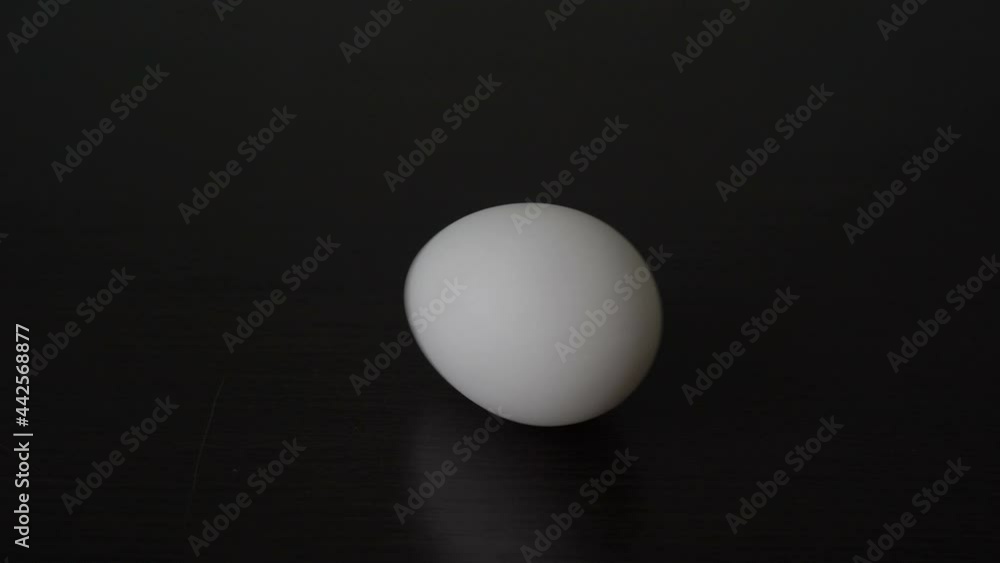 Close-up, a man's hand begins to rotate a white chicken egg that is lying on a black table. Conceptual realism. Copy space. 4K. Close-up, a man's hand begins to rotate a white chicken egg that is lying on a black table. Conceptual realism. Copy space. 4K.