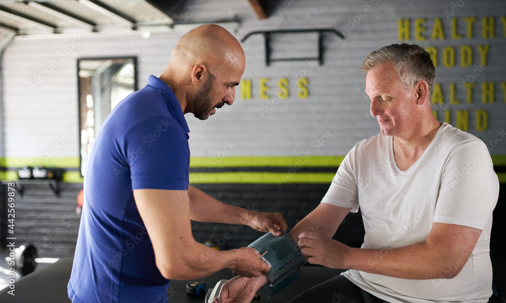 Obraz premium Male personal trainer measuring senior, elderly man's blood pressure