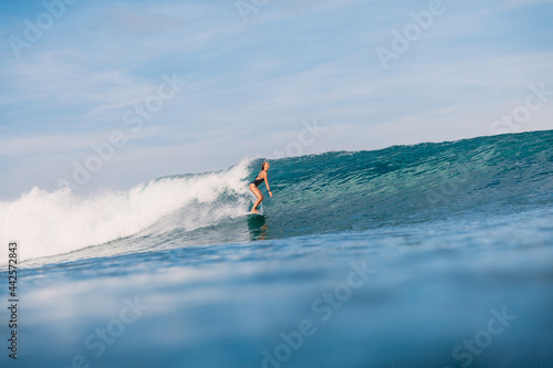 Surfer girl at surfboard on blue wave. Sporty woman in ocean surfing.
