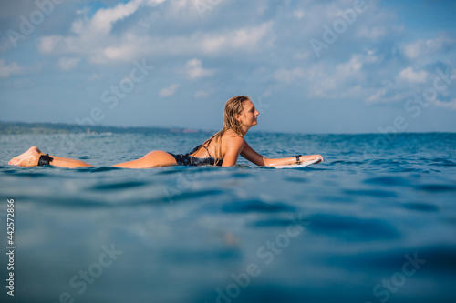 Attractive surfing woman with surfboard. Surfer girl posing on surfboard in ocean