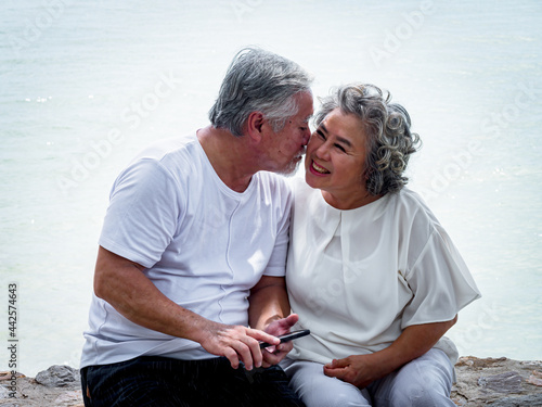 Fotografija An elderly Asian husband kisses his wife on the cheek as they head to the sea to celebrate their wedding anniversary