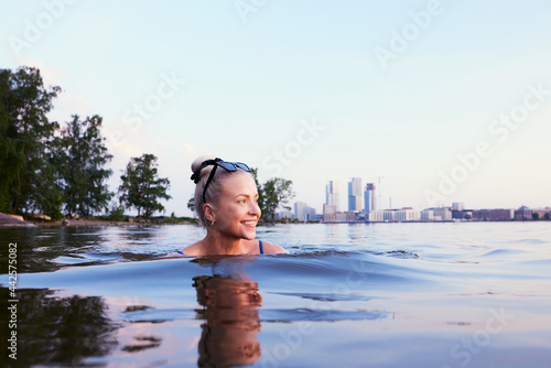 A beautiful smiling woman girl swimming in sea in helsinki Kalasatama behind her summer during evening twilight sunlight sunset in nordic green city travel tips photo