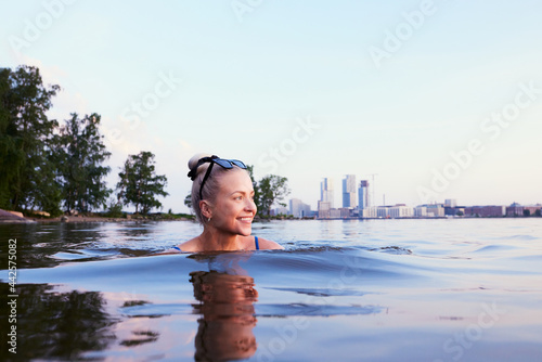 A beautiful smiling woman girl swimming in sea in helsinki Kalasatama behind her summer during evening twilight sunlight sunset in nordic green city travel tips