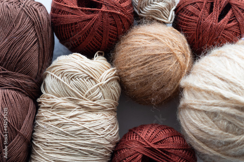 Balls of various yarns for knitting woolen nylon and acrylic of different shapes in classic colors of brown and beige in the whole frame on a white woven background handmade knitting and hobbies