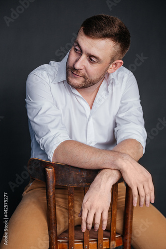 A portrait of a man sits on a chair and looks away