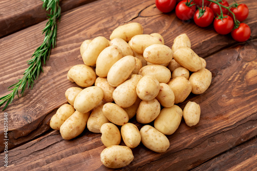 Foto Raw young small potato with rosemary and cherry tomatoes on wooden background