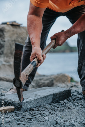 showing a stone craftsman using a pick on a slab of cancagua, in the coast of Ancud on Chiloe Island.