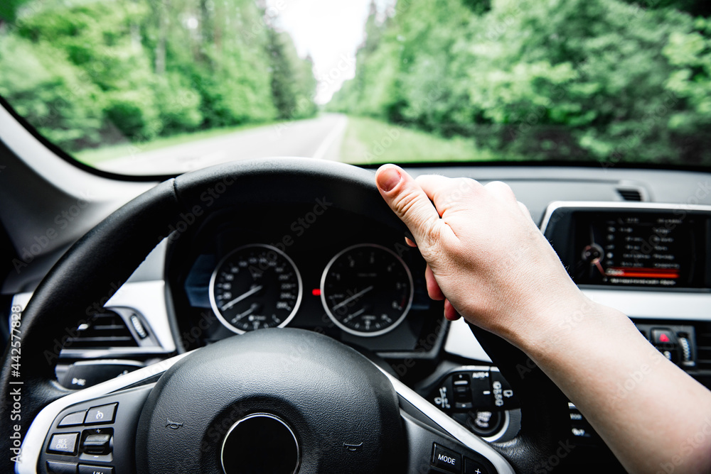 Driver's hand on steering wheel on forest background. Driving car concept.
