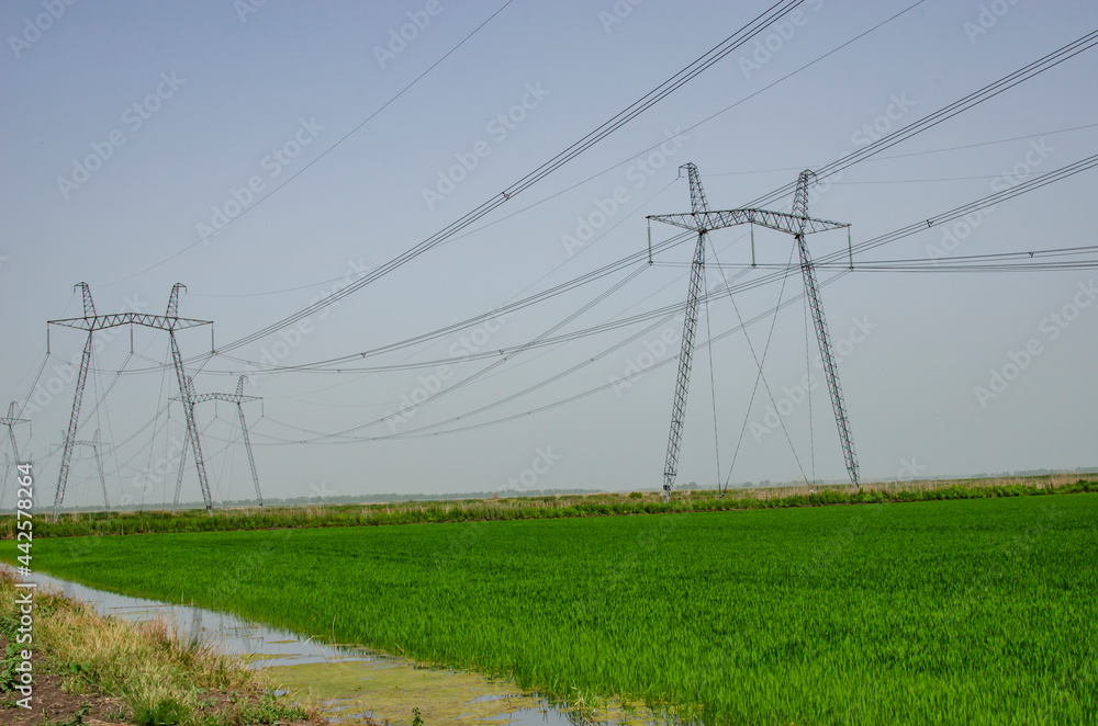 High voltage electricity line against the background of the sky and green field.