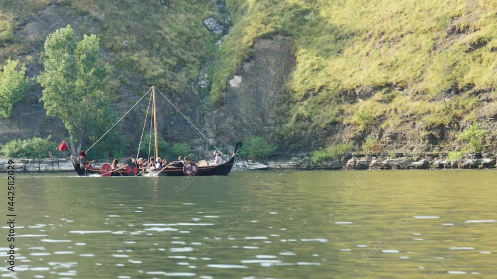 Vikings Sail on an Old Ship Along a Quiet River Against the Backdrop of a Rocky Coast. The Men Row the Oars Diligently Towards Adventure. Medieval Reconstruction.
