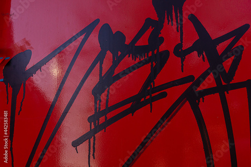 metal surface of the wall painted in red is covered with smeared traces of black paint, vandalism in the urban environment.