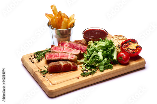 Grilled sliced roated beef steaks, potato and sauce on wooden cutting board photo