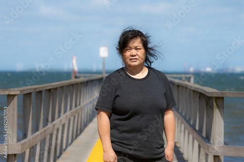 An Asian middle aged woman on a jetty with a blue ocean and sky in the background. Picture from Scania county, Sweden © Dan
