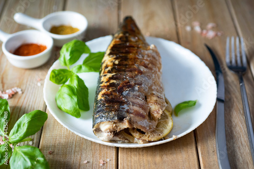 Delicious lunch: grilled mackerel with lemon, herbs and onions on a white plate on a wooden table.