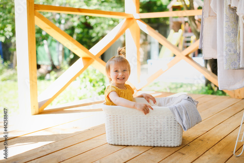Fotografia cute caucasian toddler girl in a basket with clean linen on the veranda, hangs u