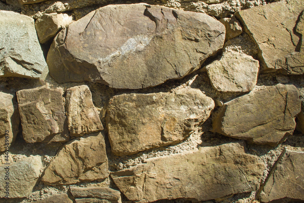 Fototapeta premium Frontal view of a wall of brown cement-bonded stones on a sunny day with deep shadows