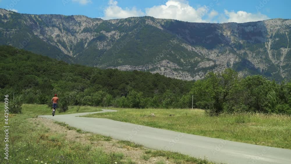 Riding a powerful electric vehicle. A man in a protective helmet rides an electric scooter in the forest against the backdrop of mountains from the camera with his back Riding a powerful electric vehicle. A man in a protective helmet rides an electric scooter in the forest against the backdrop of mountains from the camera with his back