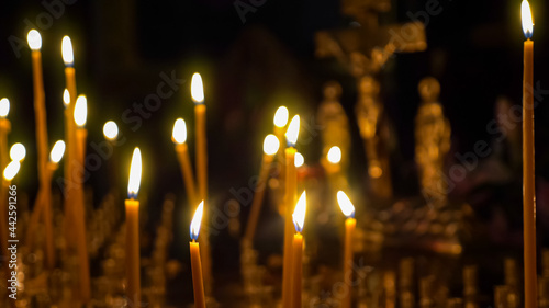 Close-up of burning wax candles against the background of a blurred crucifix in a christian temple.