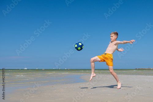 Happy teen boy playing with ball on beach at summer sunny day with blue sky